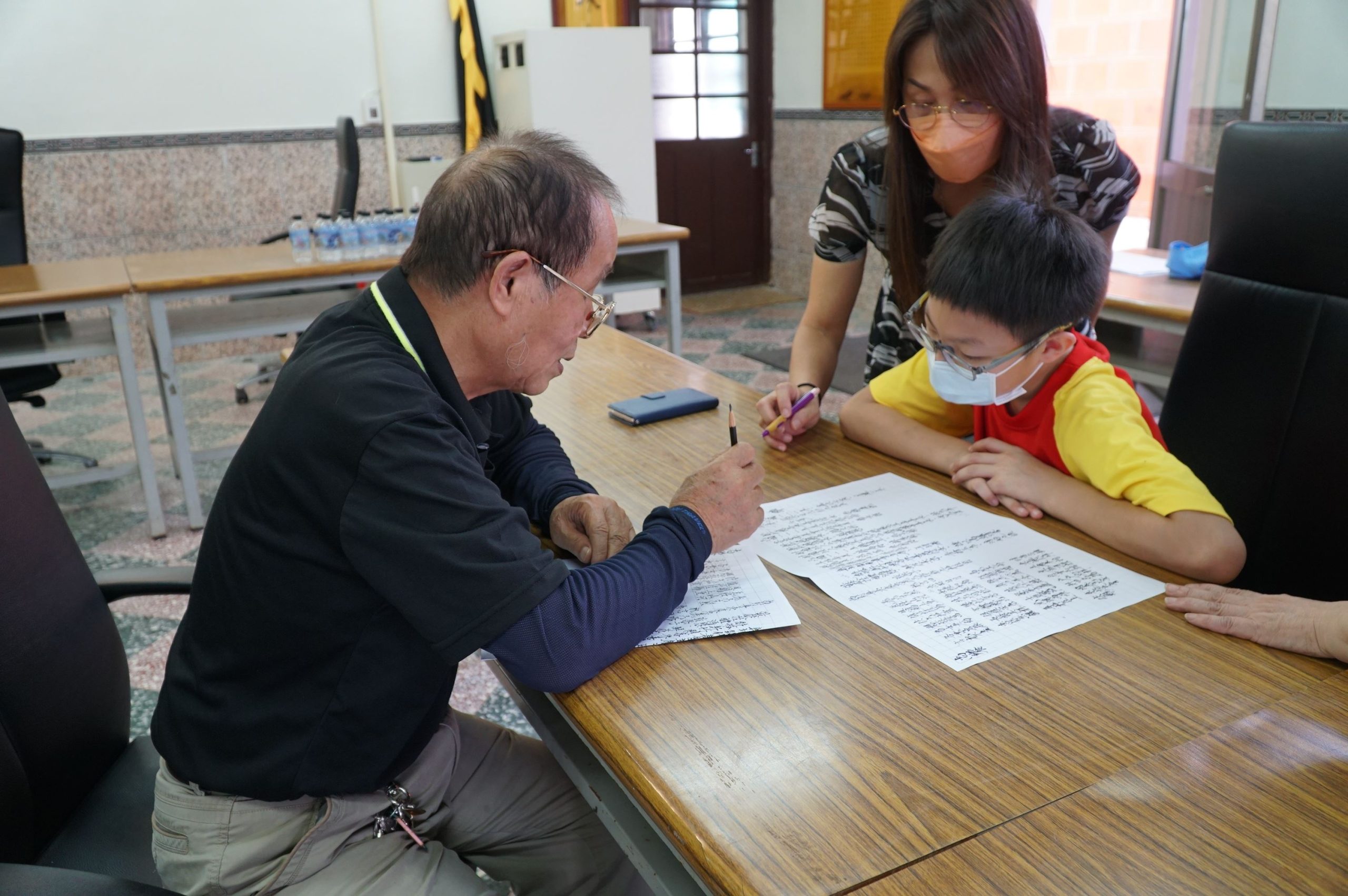 義民廟的廟公林邦雄（左）細心指點學生，以標準海陸腔客語唸祝禱文。新竹縣政府提供