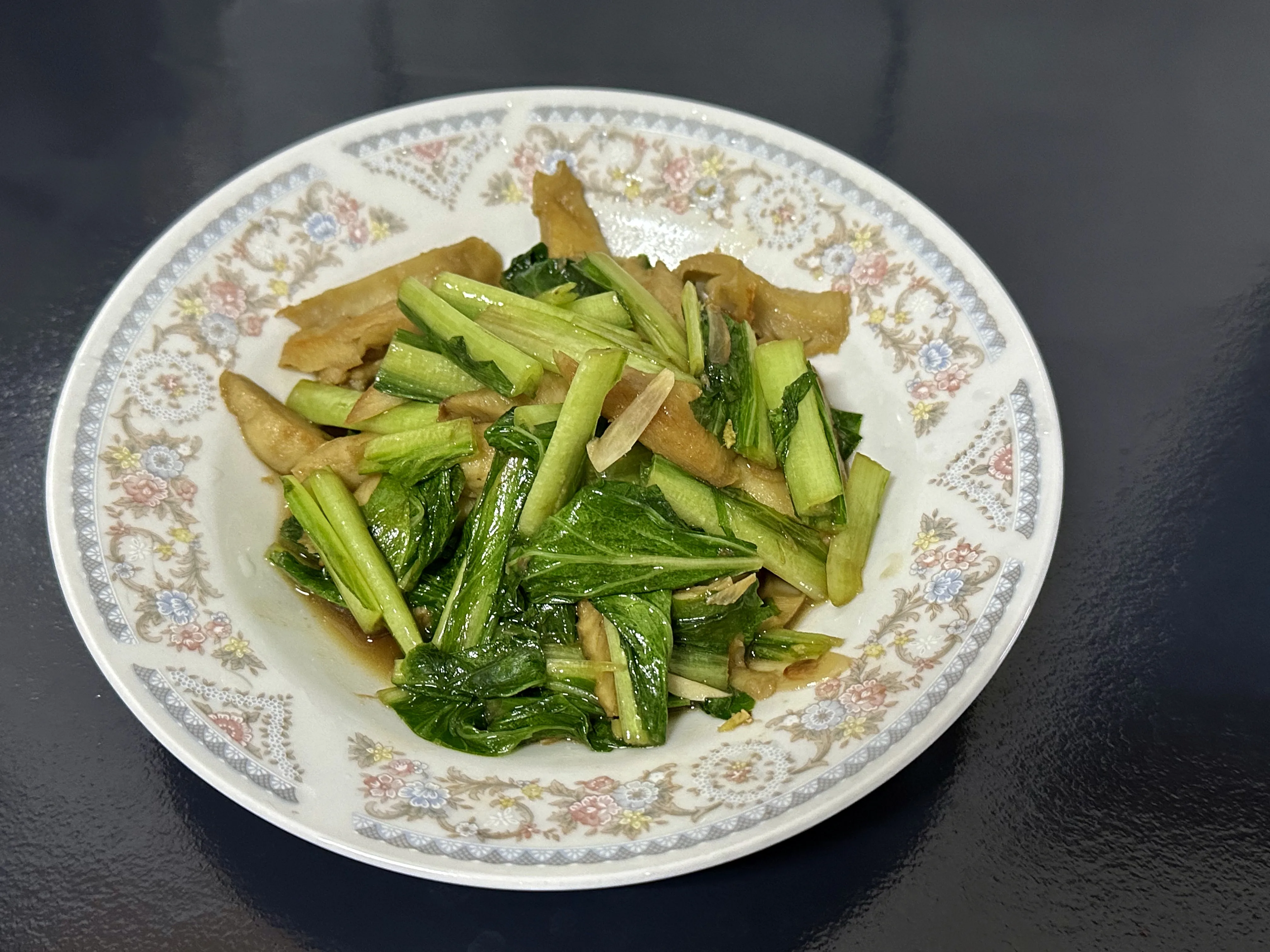 新品種的蕒仔(劍葉萵苣)炒麵筋,以蒜片與麻油提味;作法,麵筋用豬油煎赤,下蒜片炒香,再把蕒仔下鍋,起鍋前以麻油沿鍋邊繞一圈,盛盤。作者提供