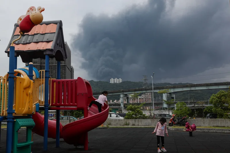 新北市泰山區南亞塑膠林口廠7日凌晨發生火警,幸無人受困。圖為小朋友在泰山區一處公園遊玩,遠處可見廠房冒出濃濃黑煙。中央社