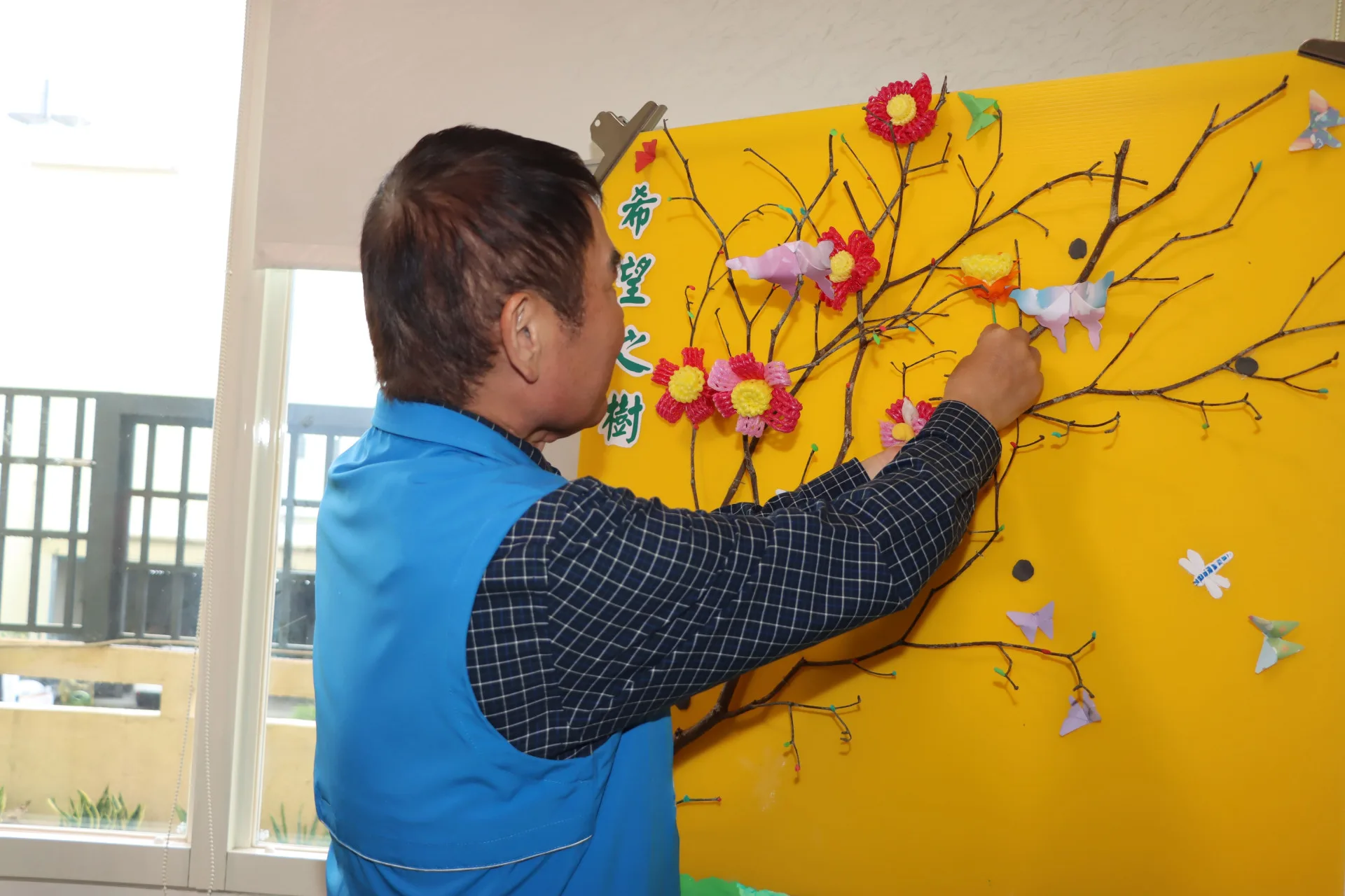 鍾東錦將花朵貼在「生命之樹」上，象徵持續拓展的身障者照顧服務據點開花結果。苗縣府提供