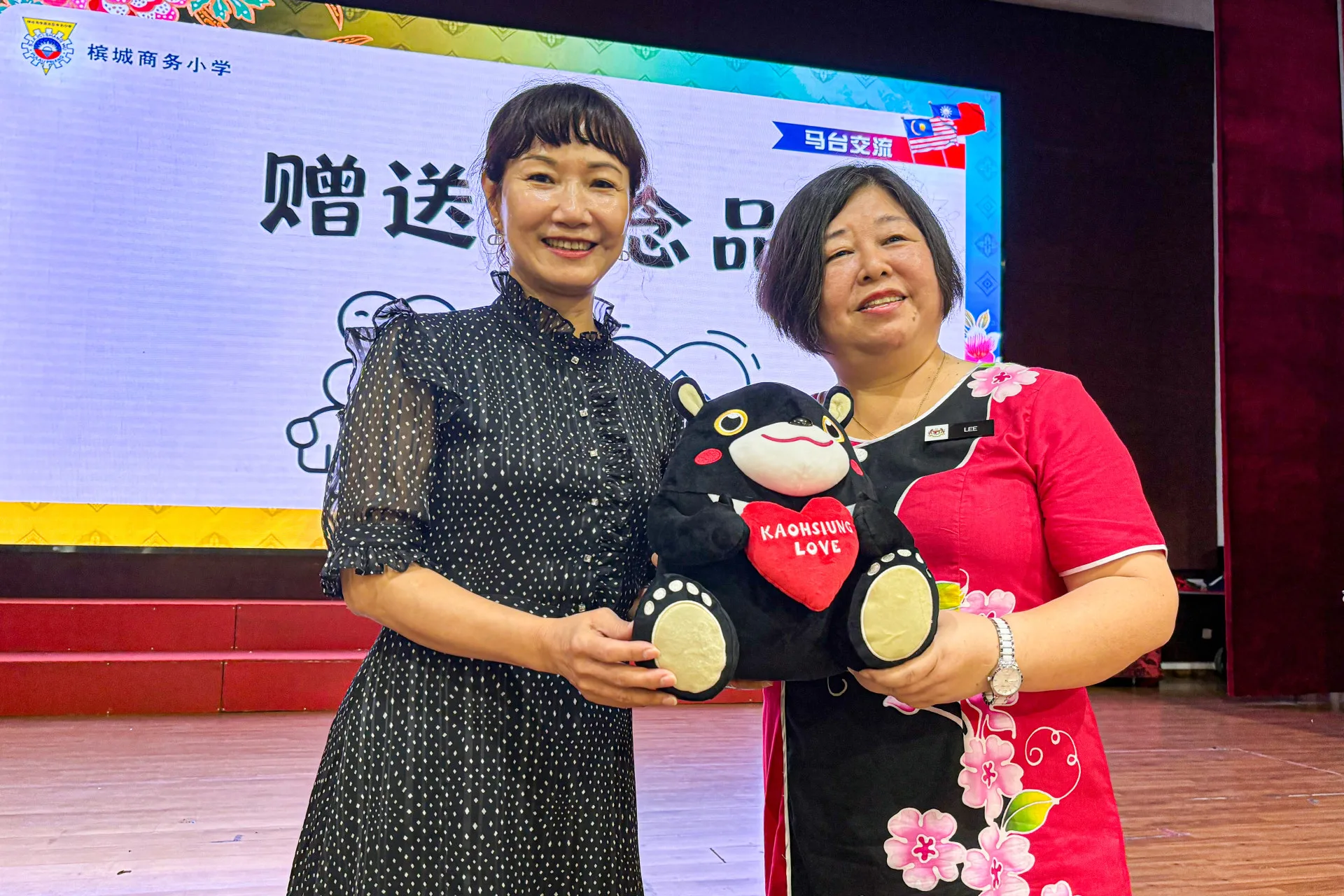 客委會主委楊瑞霞(左)代表高雄市長陳其邁致贈吉祥物高雄熊紀念品給商務華小校長李鳳珠(右)。高雄市客委會提供