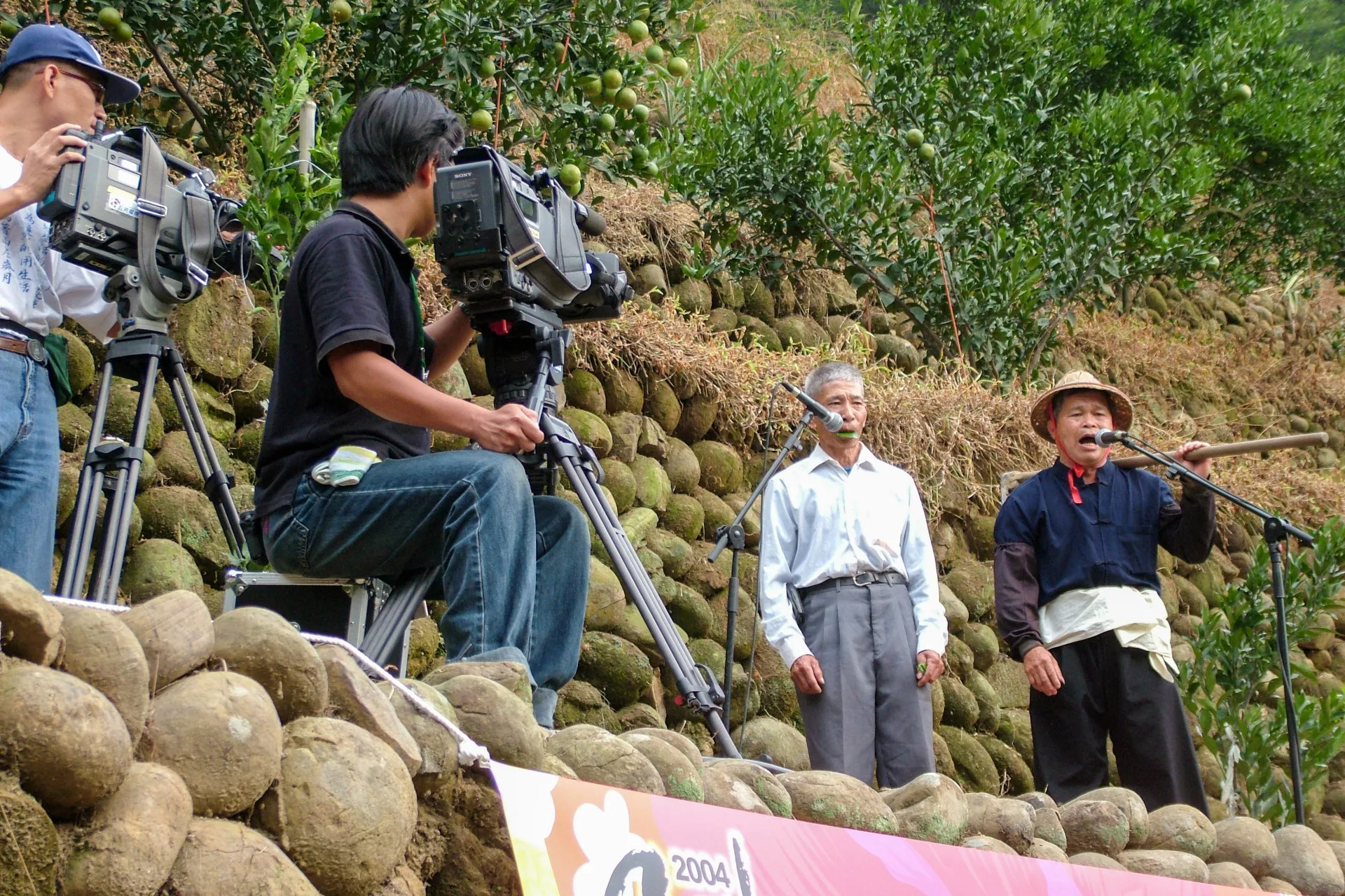 2004年在新竹縣芎林鄉鹿寮坑舉辦的地景音樂會,林德富(右)擔綱演出原生態山歌,與在數十公尺外的彭六妹對唱山歌,當時的客委會主委羅文嘉到場欣賞後是讚譽有加。楊國鑫攝