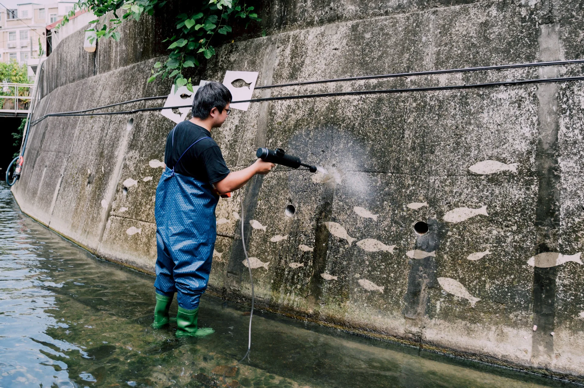 以高壓水槍洗去水圳溝壁的髒汙，顯現出特定圖案的洗垢藝。陳安嘉攝