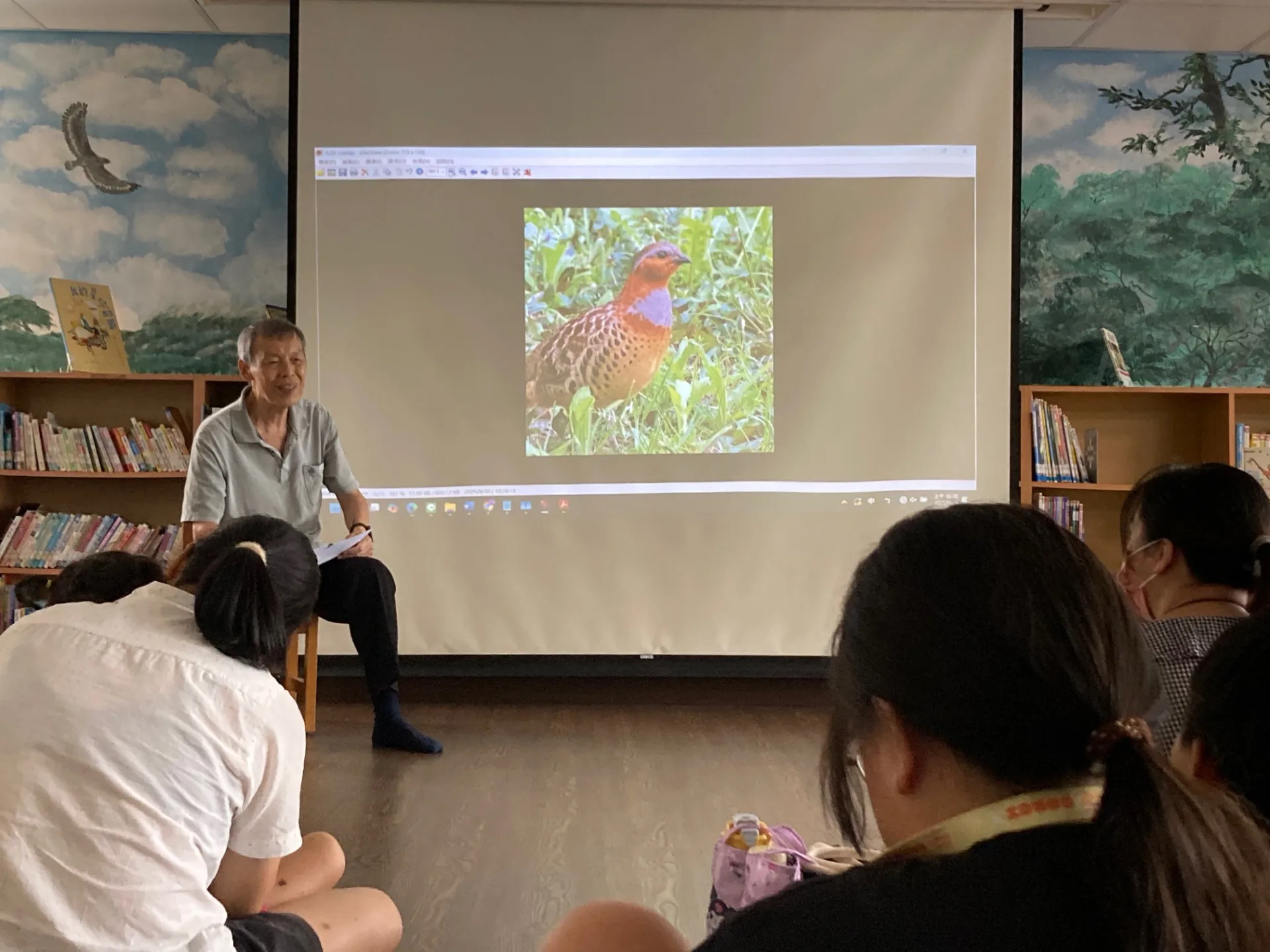 投影螢幕上出現大卷尾照片，馮輝岳用生動影像帶入童謠故事情境。