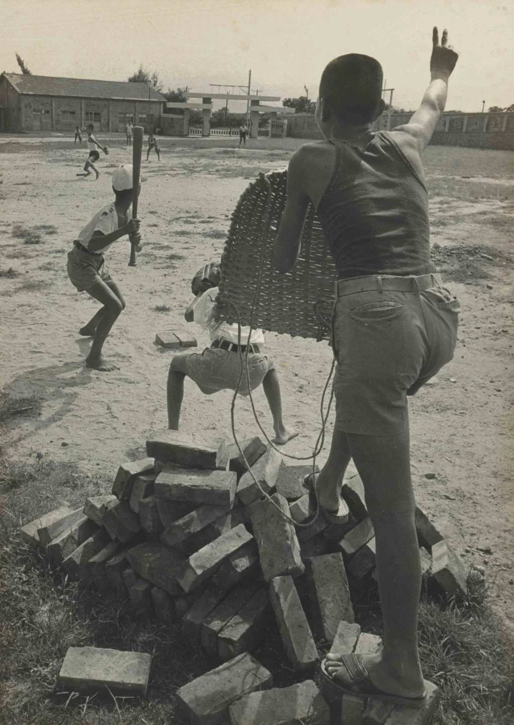棒球是參與門檻很高的運動，1970年代之前，參與棒球只能靠著自己的雙手發揮巧思，製作各種打球時需要的裝備。例如照片中用畚箕當作是主審的護胸裝備。早年棒球隊把學校操場或是空地當作是棒球場，在如此克難的環境下，赤著腳在逆境下闖出一片天。攝影家邱德雲作品。國家攝影文化中心提供