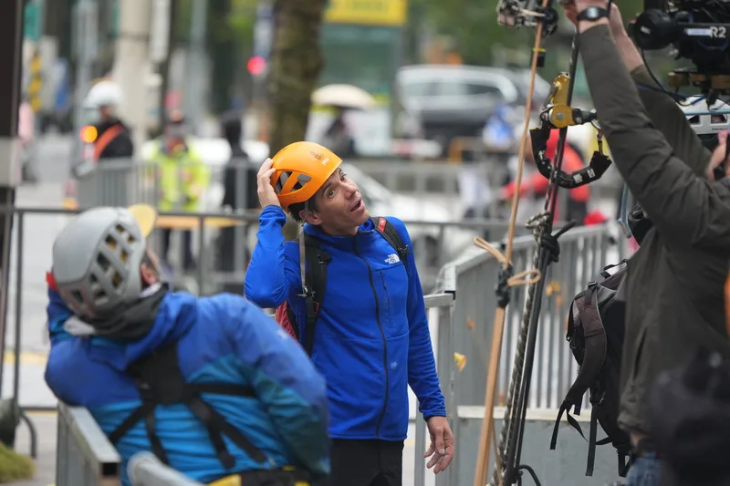 美國自由攀岩好手霍諾德（Alex Honnold）將於台灣時間24日以徒手攀登的方式，挑戰台北101大樓並全程直播。圖為霍諾德（中）21日雨天試爬前與團隊交換意見。中央社