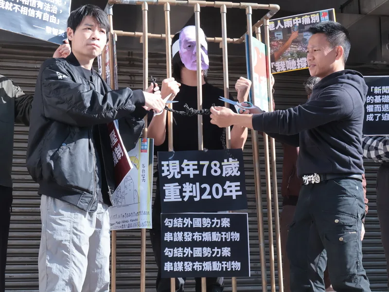 民團、在台港人、台灣新聞記者協會、無國界記者組織、台灣青年世代共好協會、經民連智庫等團體與個人10日上午在立法院群賢樓前聲援香港壹傳媒創辦人黎智英被控違反香港國安法、遭判20年一案，香港邊城青年秘書長馮詔天（左）、在台港人湯偉雄（右）現場演出行動劇。中央社