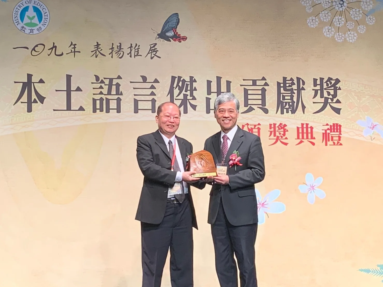 張義品（左）於2020年榮獲教育部本土語言傑出貢獻獎，他從客委會前副主委范佐銘手中接下獎座。客家雜誌提供