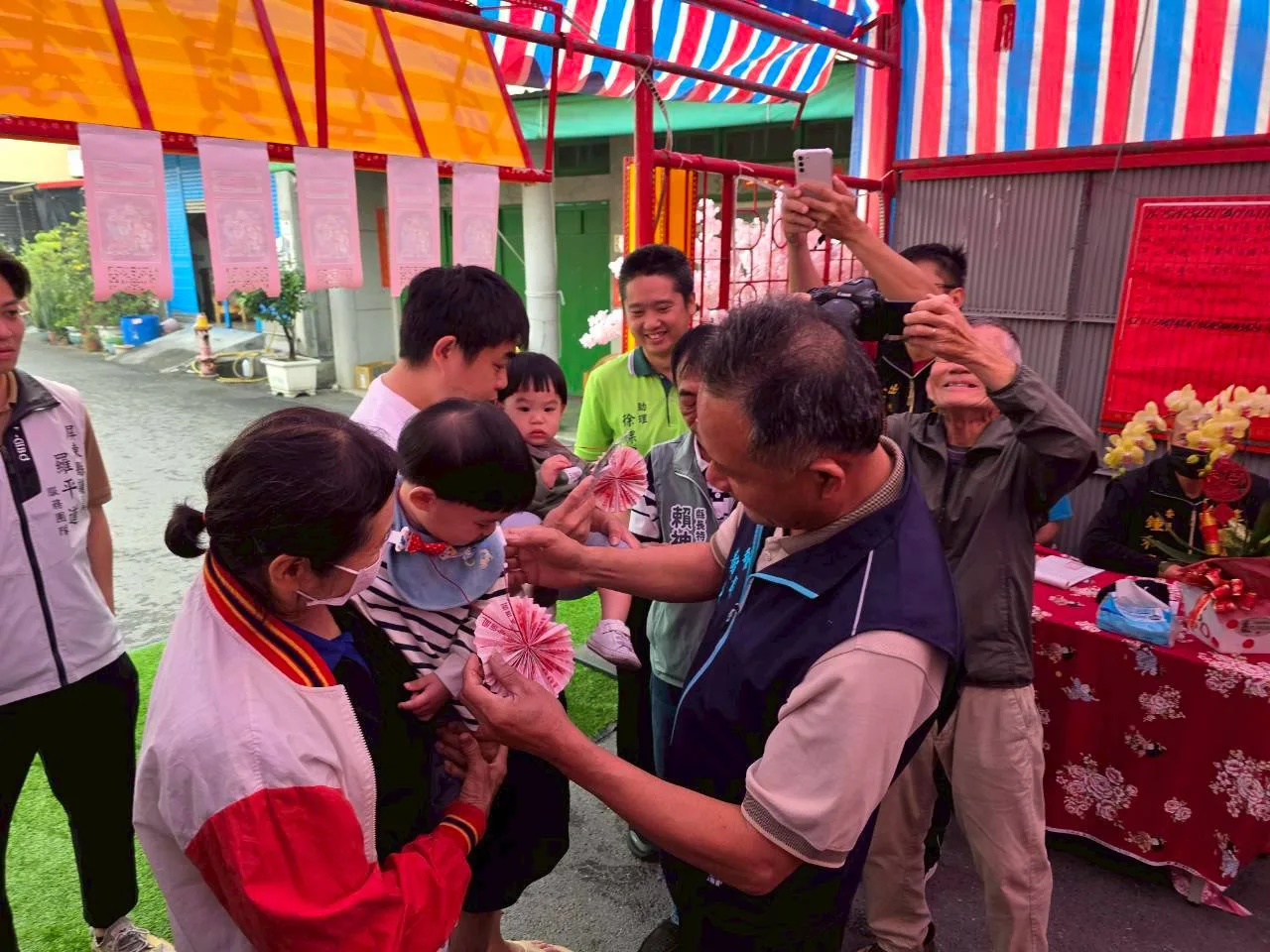 將新台幣摺成圓形，以紅繩掛在新丁頭胸前，象徵圓滿，稱為「結衫帶」。佳冬鄉公所提供