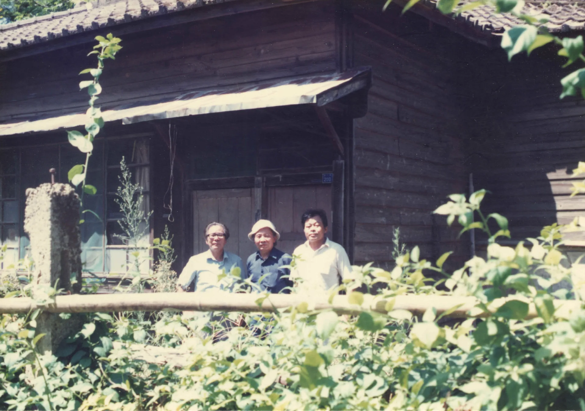 我帶多位文友，參觀芎林國小，鄧雨賢過世後，後來日本人離開了，鄧雨賢家族就住在這個日本宿舍。友人在宿舍前留影，左為鍾孝上，中為鍾肇政，右為黃榮洛。1988，芎林，楊國鑫攝