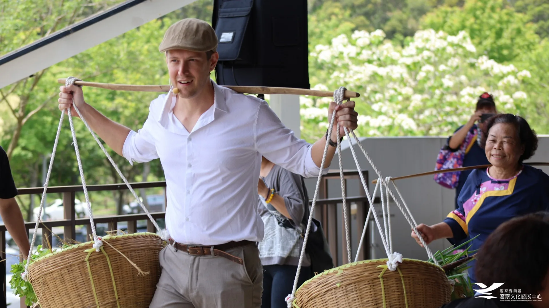 美籍歌手賈斯汀與苗栗在地大襟客文化藝術團成員，挑著宴席所使用的在地食材入場。客發中心提供